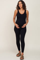 woman wearing a black maternity jumpsuit showing her baby bump and posing with hands on her stomach
