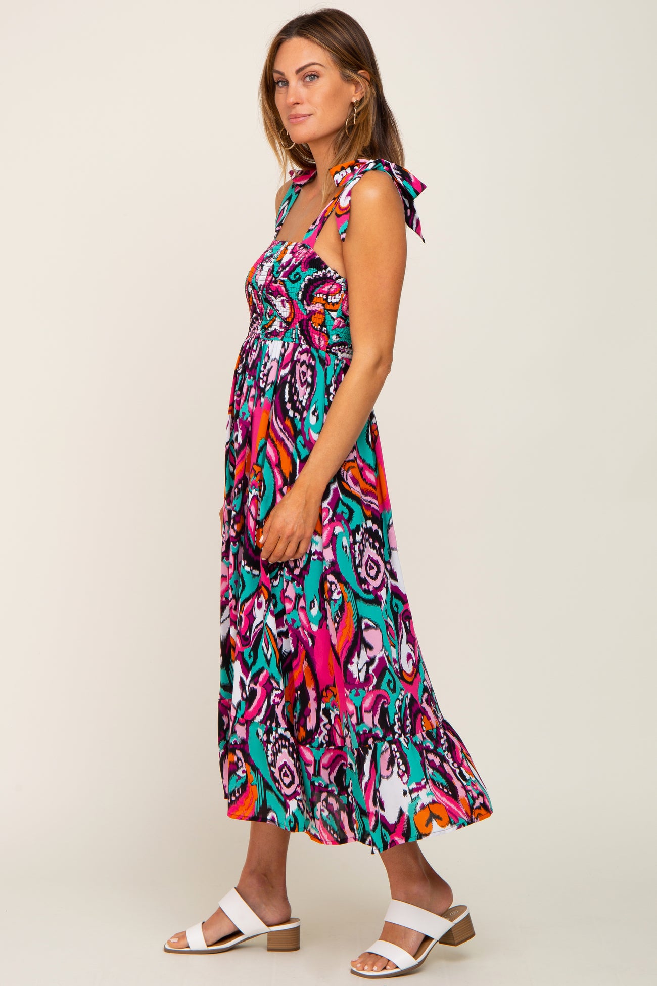 woman wearing a colorful maxi dress with tie straps and a flowing skirt, styled with white sandals