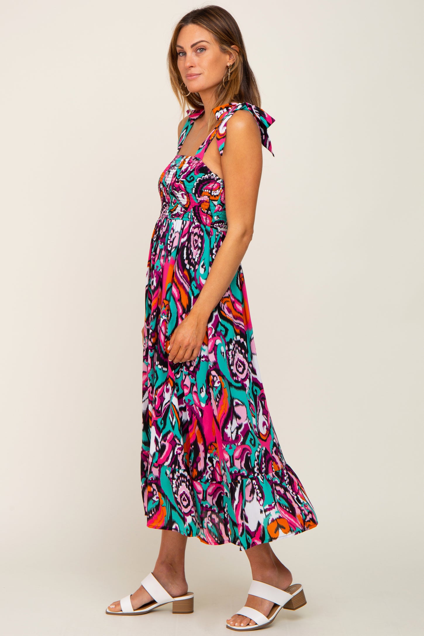 woman wearing a colorful maxi dress with tie straps and a flowing skirt, styled with white sandals