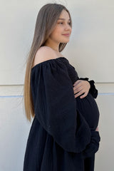 pregnant woman with long brown hair wearing a black off-the-shoulder maternity dress holding her baby bump