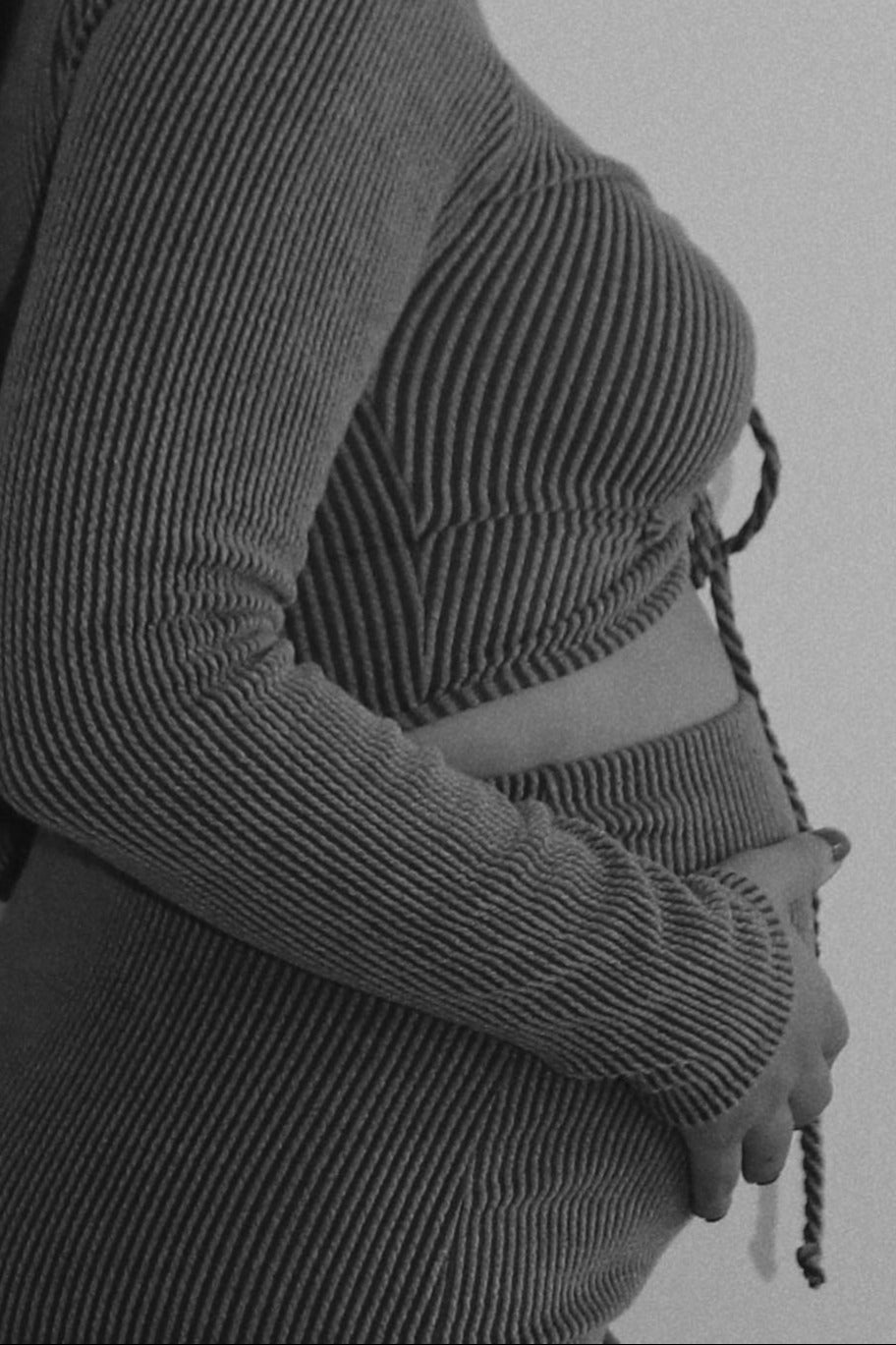 Black and white side profile of a pregnant person wearing a ribbed knit maternity set holding their baby bump