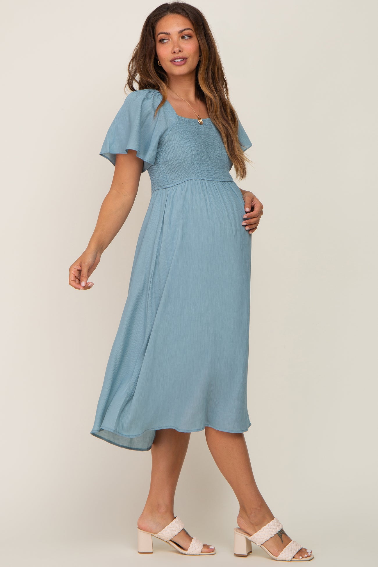 woman wearing a light blue maternity dress with short flutter sleeves and a smocked bodice, showcasing her baby bump