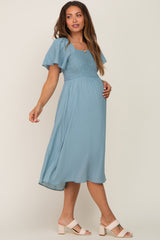 woman wearing a light blue maternity dress with short flutter sleeves and a smocked bodice, showcasing her baby bump