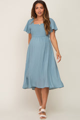 woman wearing a blue maternity dress with flutter sleeves and a smocked waist, showcasing her baby bump