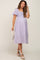 woman wearing a lavender maternity dress with short sleeves and a fitted bodice, gently cradling her baby bump