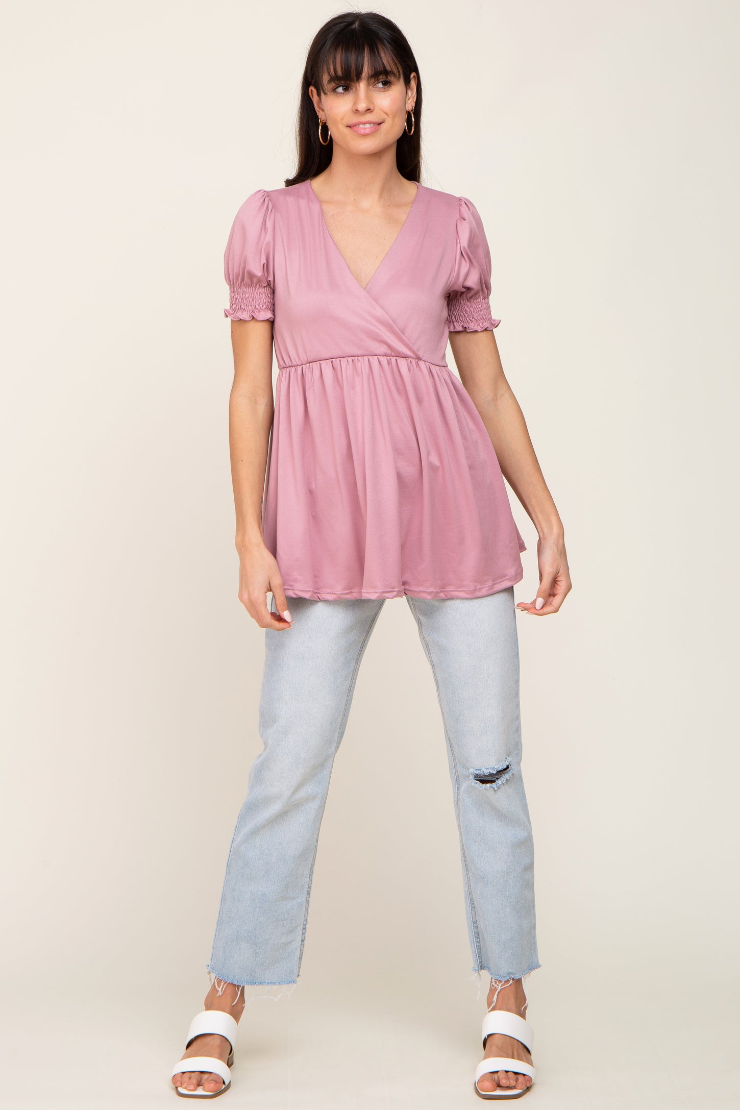 woman wearing a rose pink peplum top with puff sleeves paired with light blue distressed jeans and white sandals