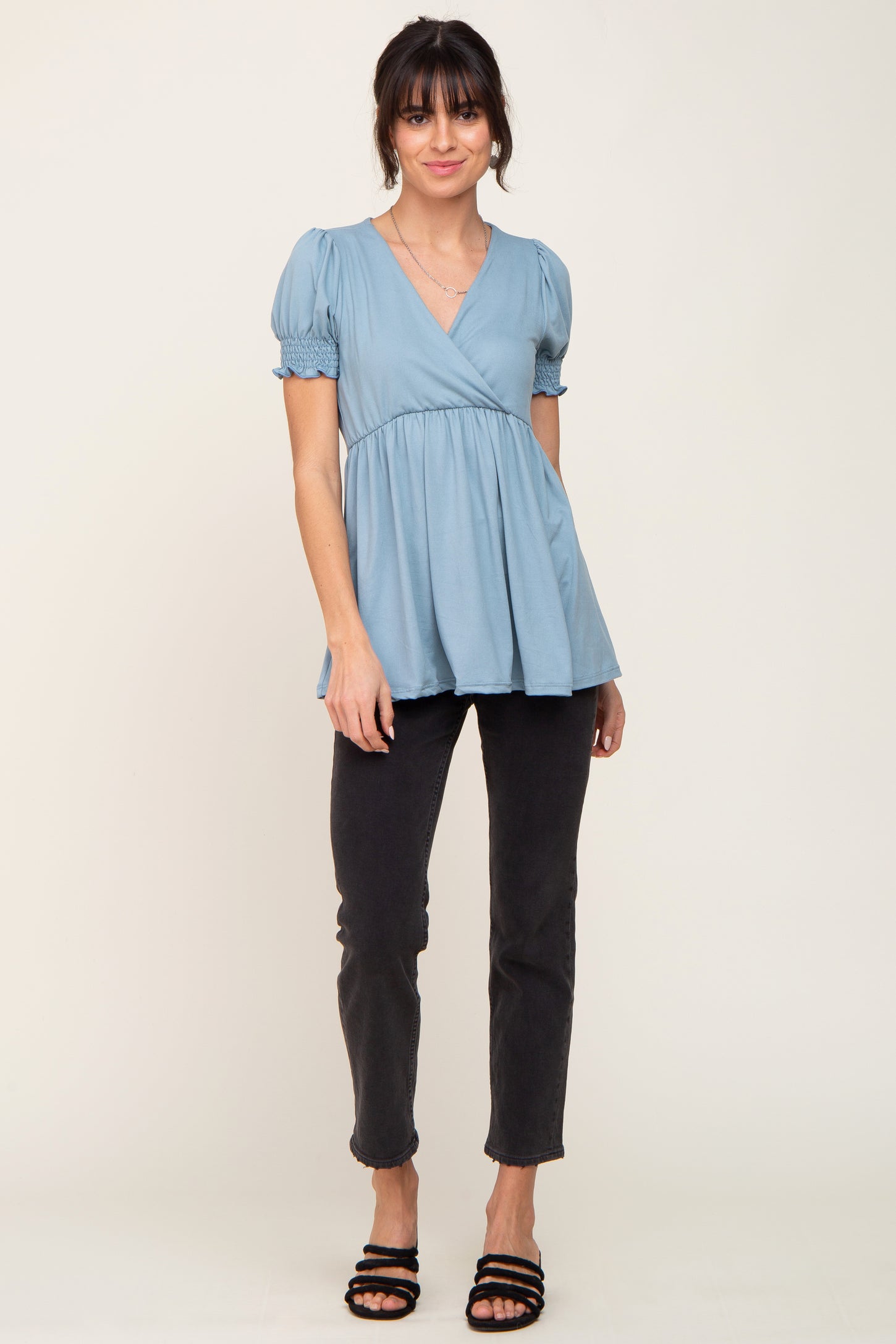 woman wearing a light blue short sleeve wrap top and black jeans with strappy sandals