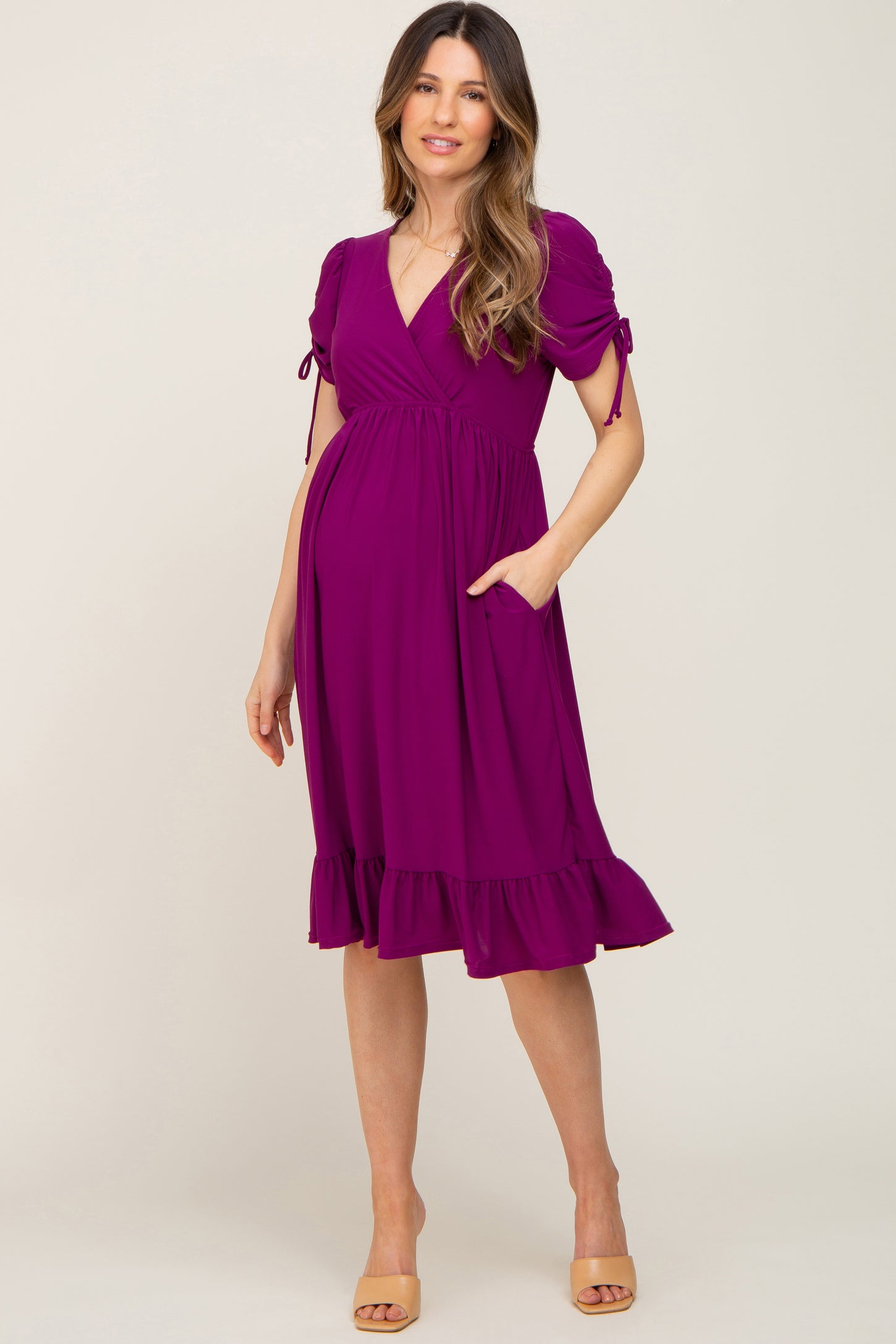 woman wearing a purple short sleeve wrap maternity dress with ruffle hem and pockets, showcasing her baby bump