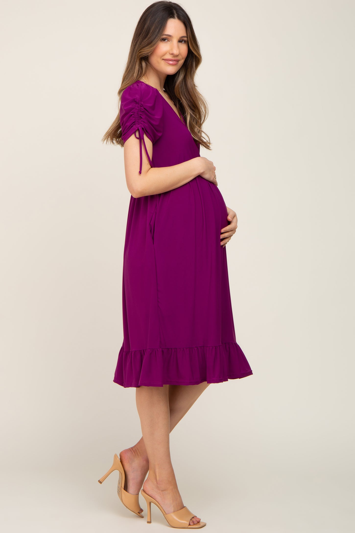 woman wearing a purple maternity dress with short puff sleeves and ruffled hem, cradling her baby bump