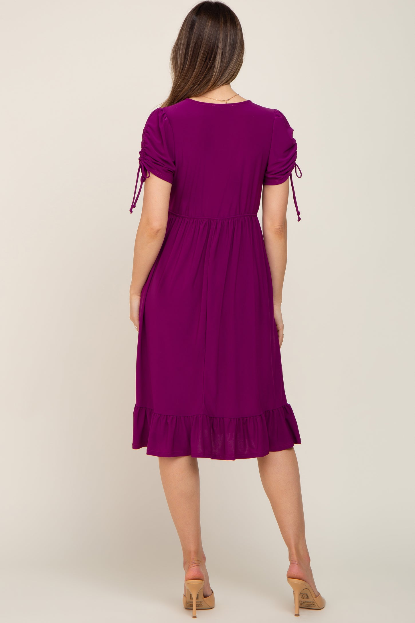 woman wearing a purple maternity dress with puff sleeves and a ruffled hem, showing her baby bump