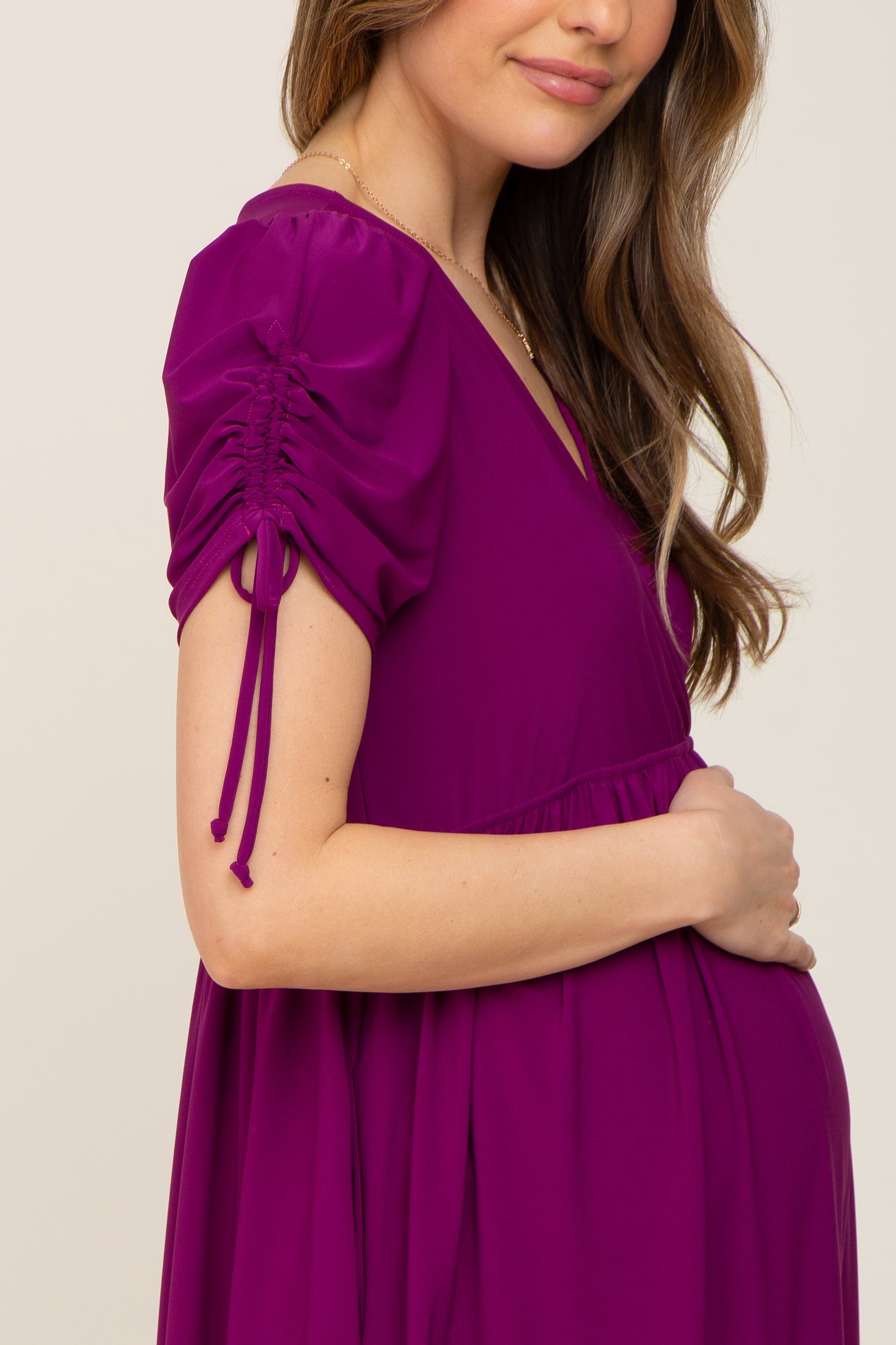 woman wearing a purple maternity dress with puff sleeves and ruching details, gently holding her baby bump