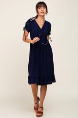 woman wearing a navy blue short sleeve dress with tie details and a ruffled hem, holding sunglasses