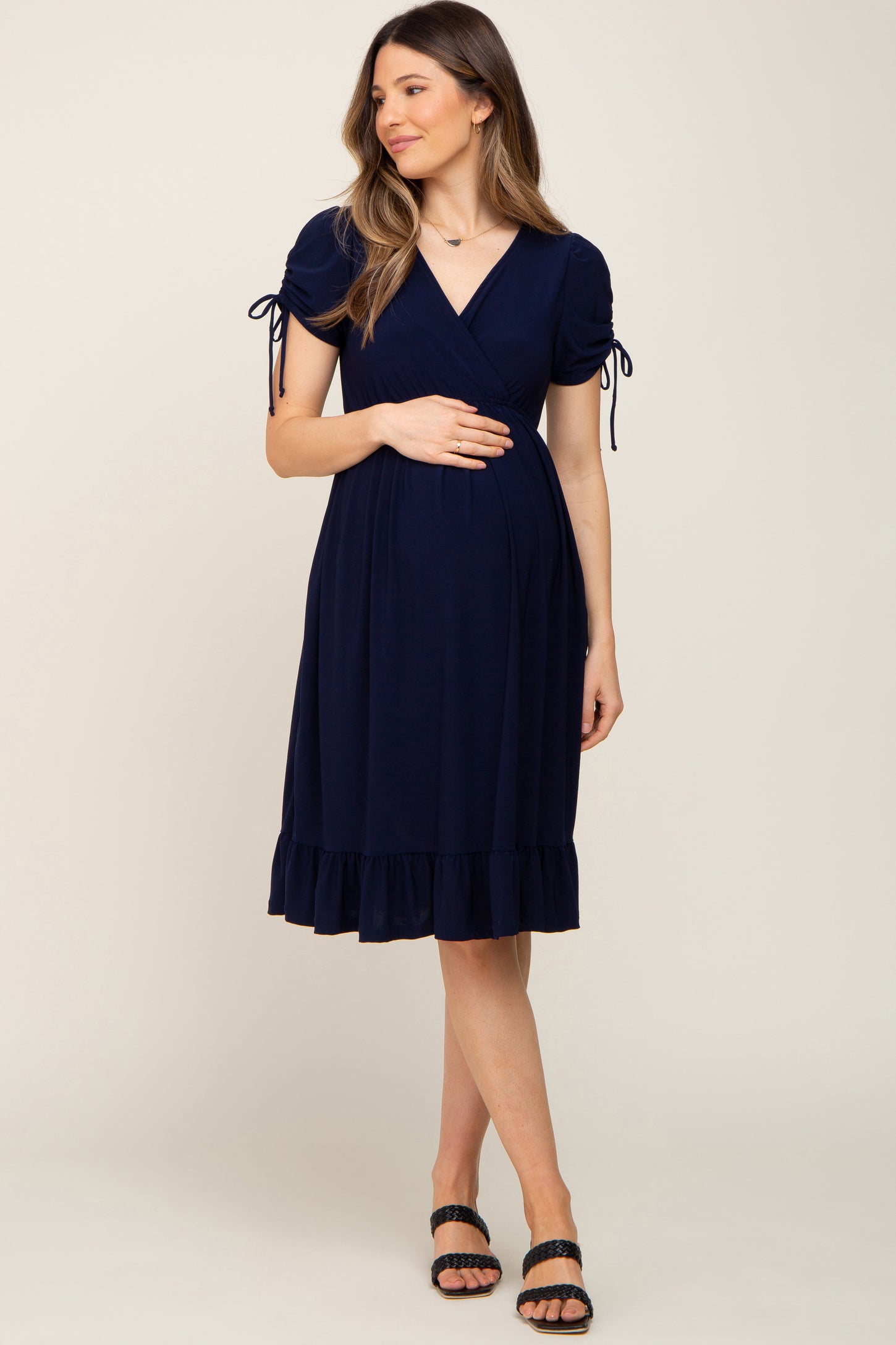 woman wearing a navy blue wrap maternity dress with short puff sleeves and a ruffled hem, holding her baby bump