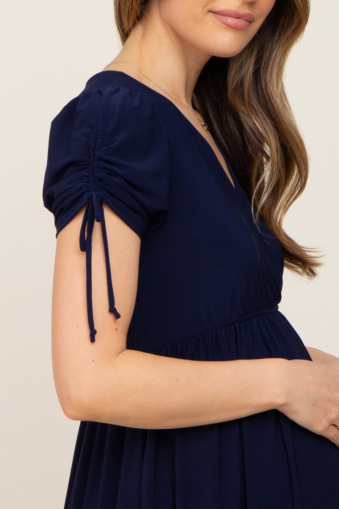 woman wearing a navy blue maternity dress with puffed sleeves and tie details, showcasing her baby bump