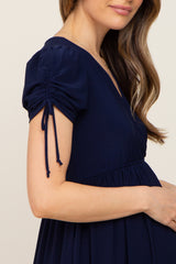 woman wearing a navy blue maternity dress with puffed sleeves and tie details, showcasing her baby bump
