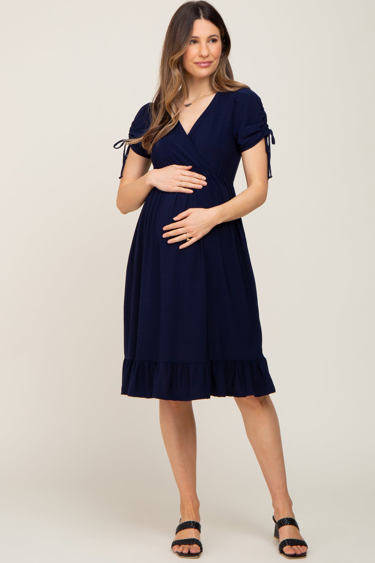 woman wearing a navy blue short sleeve maternity wrap dress with a ruffled hem and holding her baby bump