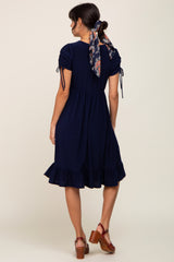 woman wearing a navy blue short sleeve dress with drawstring details and a ruffled hem, styled with a scarf in her hair