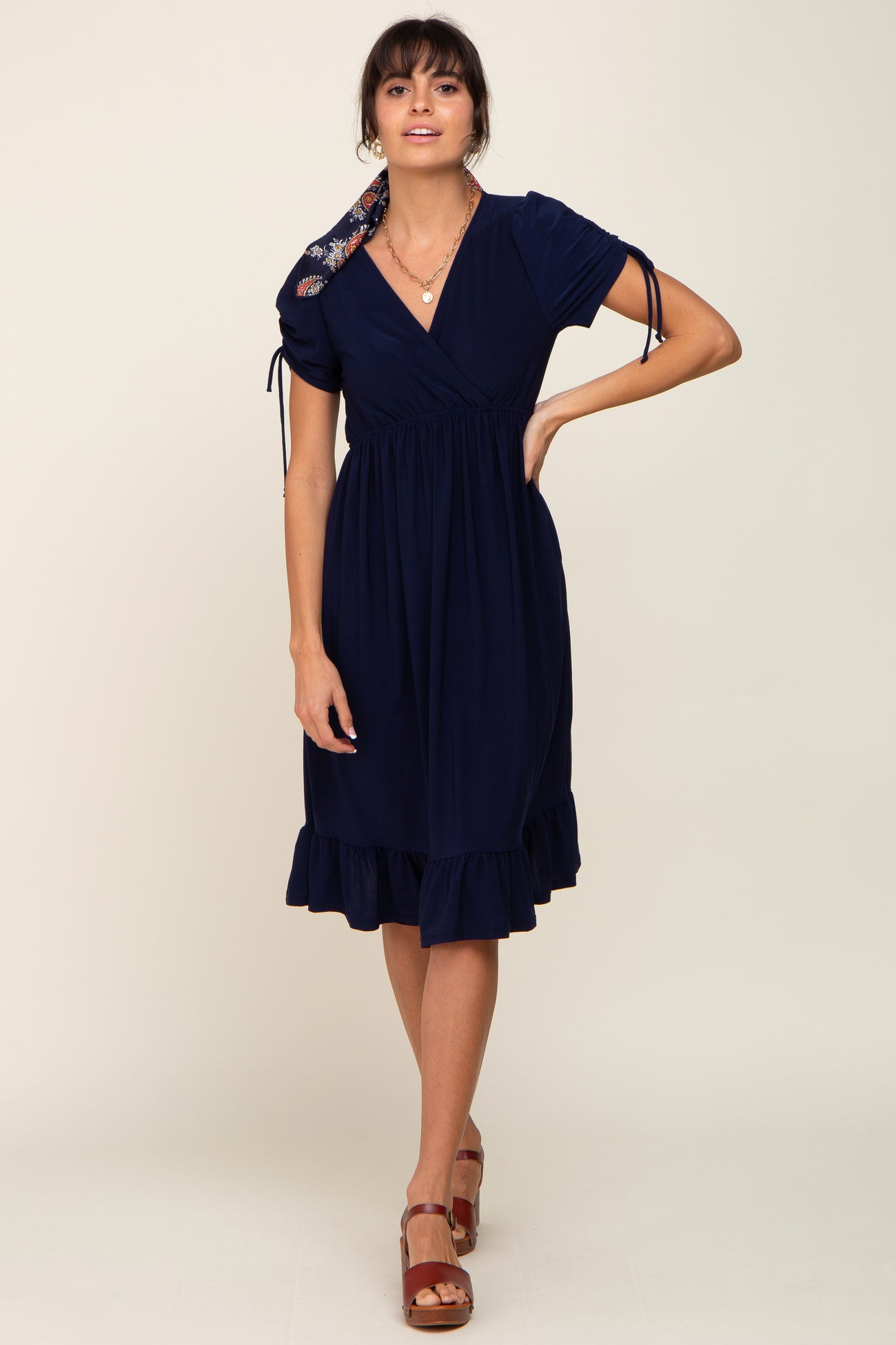 woman wearing a navy blue short sleeve wrap dress with ruffled hem and floral tie detail on the shoulder