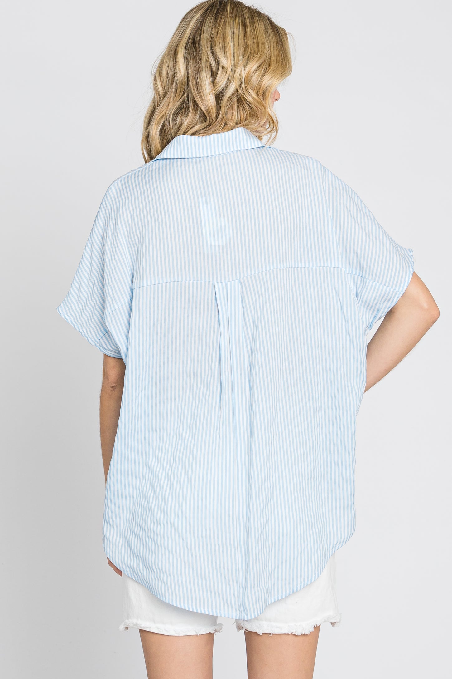 back view of woman wearing light blue and white striped short sleeve button down shirt with white shorts