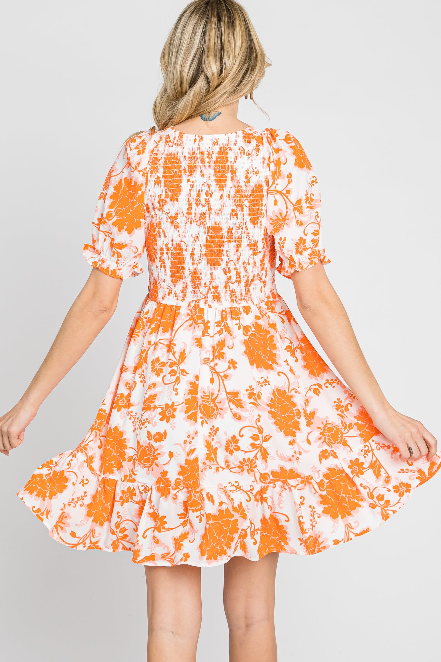 Back view of woman wearing orange and white floral print mini dress with smocked bodice and ruffled hem