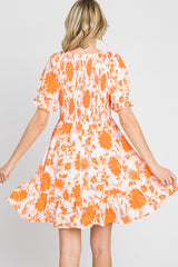 Back view of woman wearing orange and white floral print mini dress with smocked bodice and ruffled hem