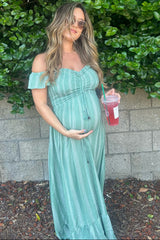woman wearing a green striped off-the-shoulder maternity maxi dress and holding a drink with her baby bump visible