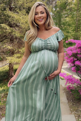 woman wearing a green striped off-the-shoulder maternity dress and holding her baby bump in a garden setting