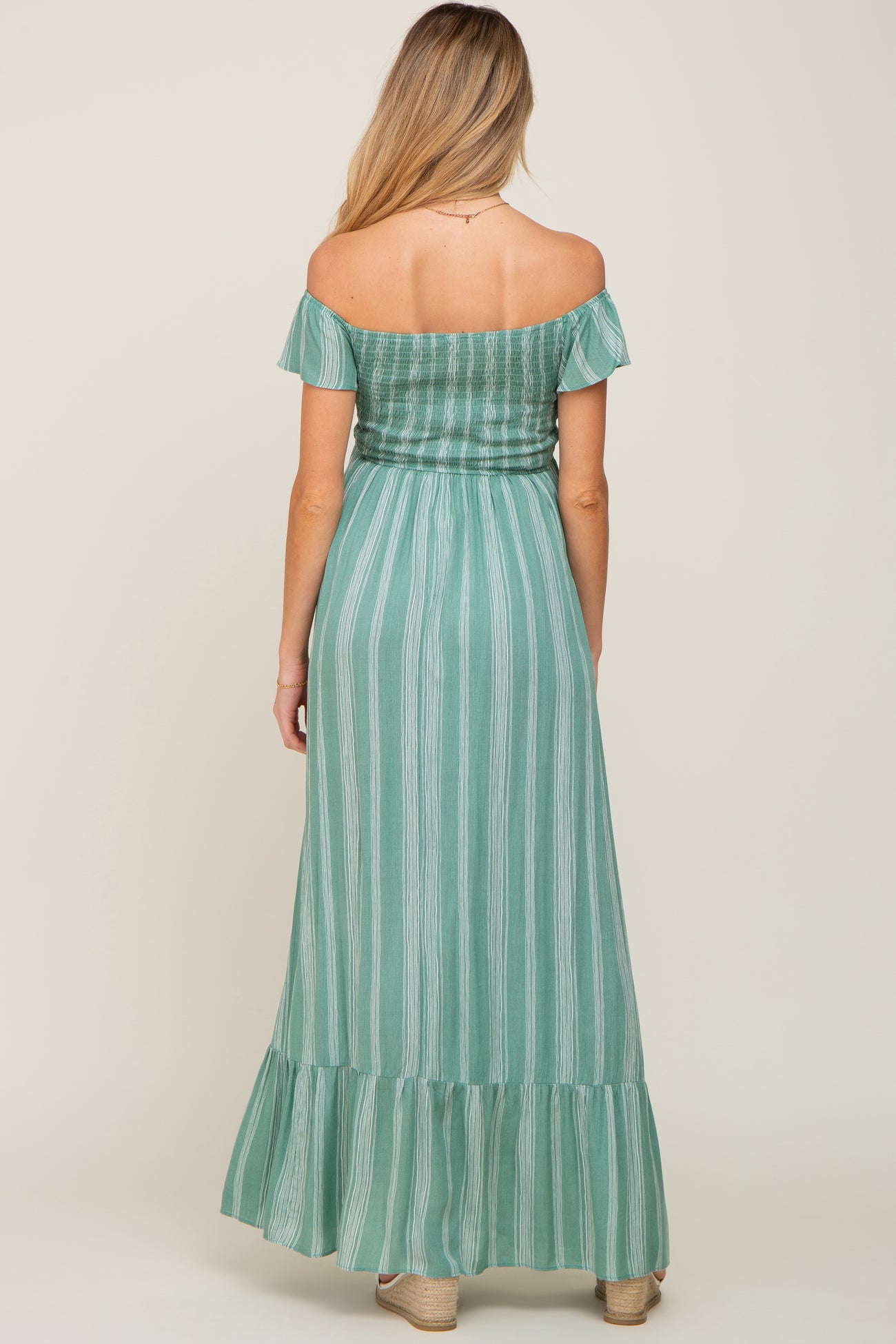 woman wearing a mint green striped off-the-shoulder maternity maxi dress with ruffle hem and smocked bodice