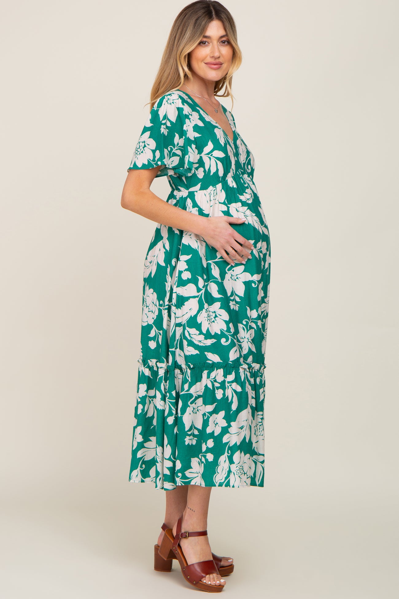 woman wearing a green floral print maternity dress and holding her baby bump