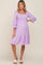 woman wearing a light purple maternity dress with a square neckline, smocked bodice, and tiered hem, highlighting her baby bump