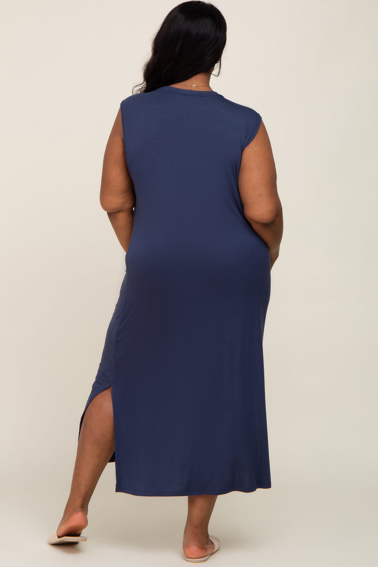 woman wearing a navy blue sleeveless maxi dress with a side slit, viewed from the back