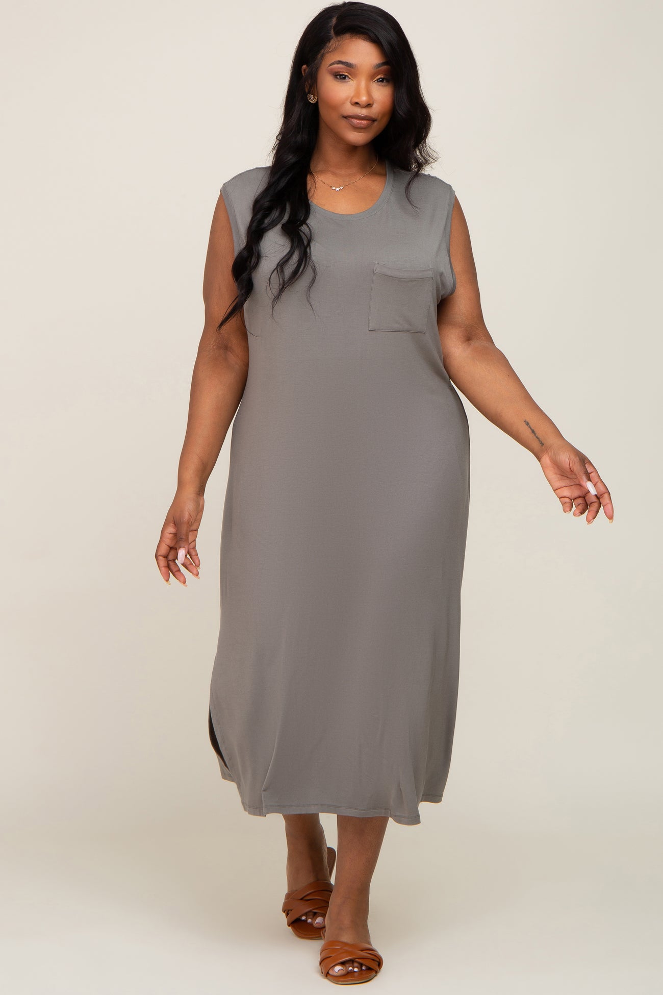 Woman wearing a sleeveless grey midi dress with a front pocket and brown slide sandals