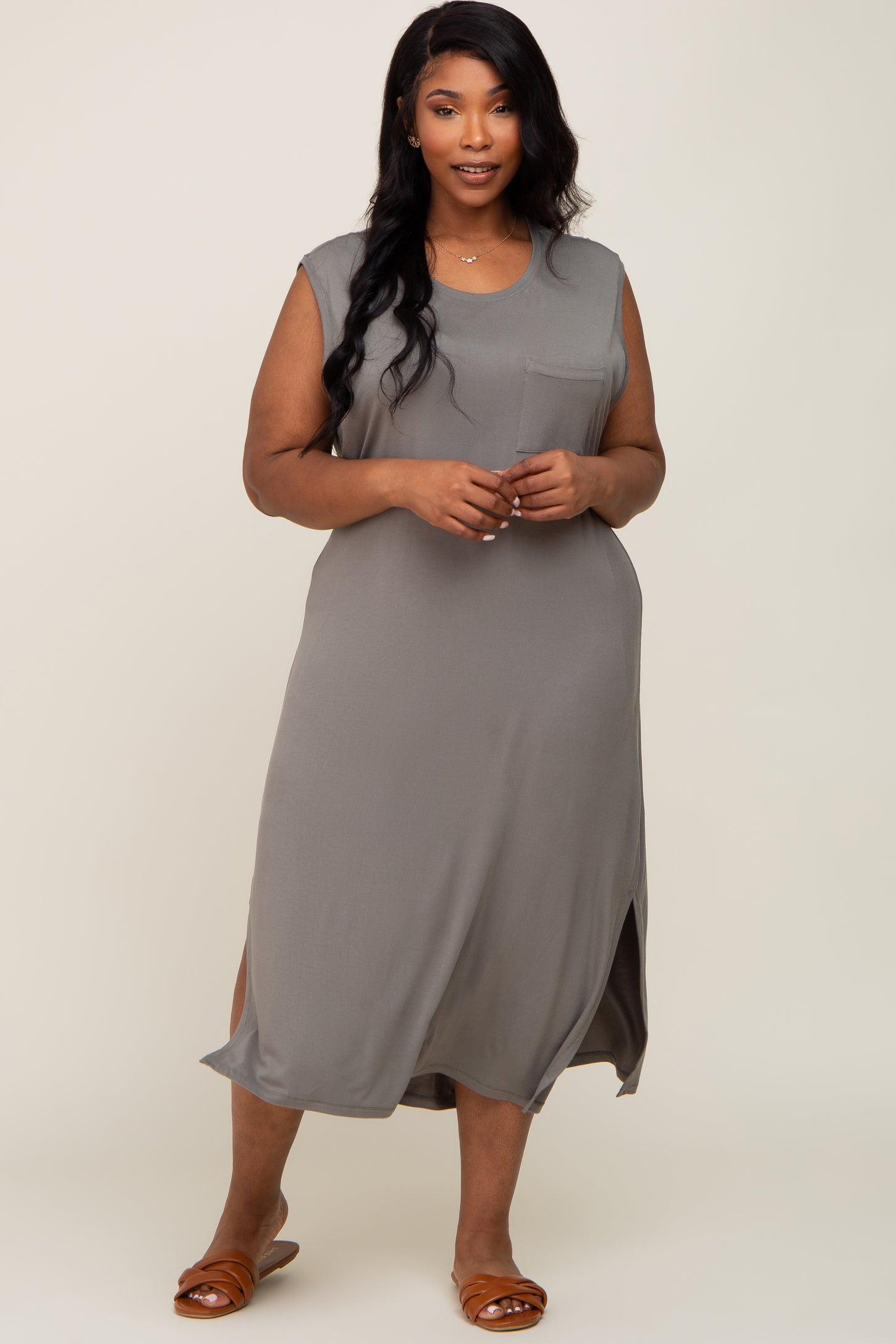 woman wearing a sleeveless gray plus-size dress with a scoop neck and side slits, standing and smiling