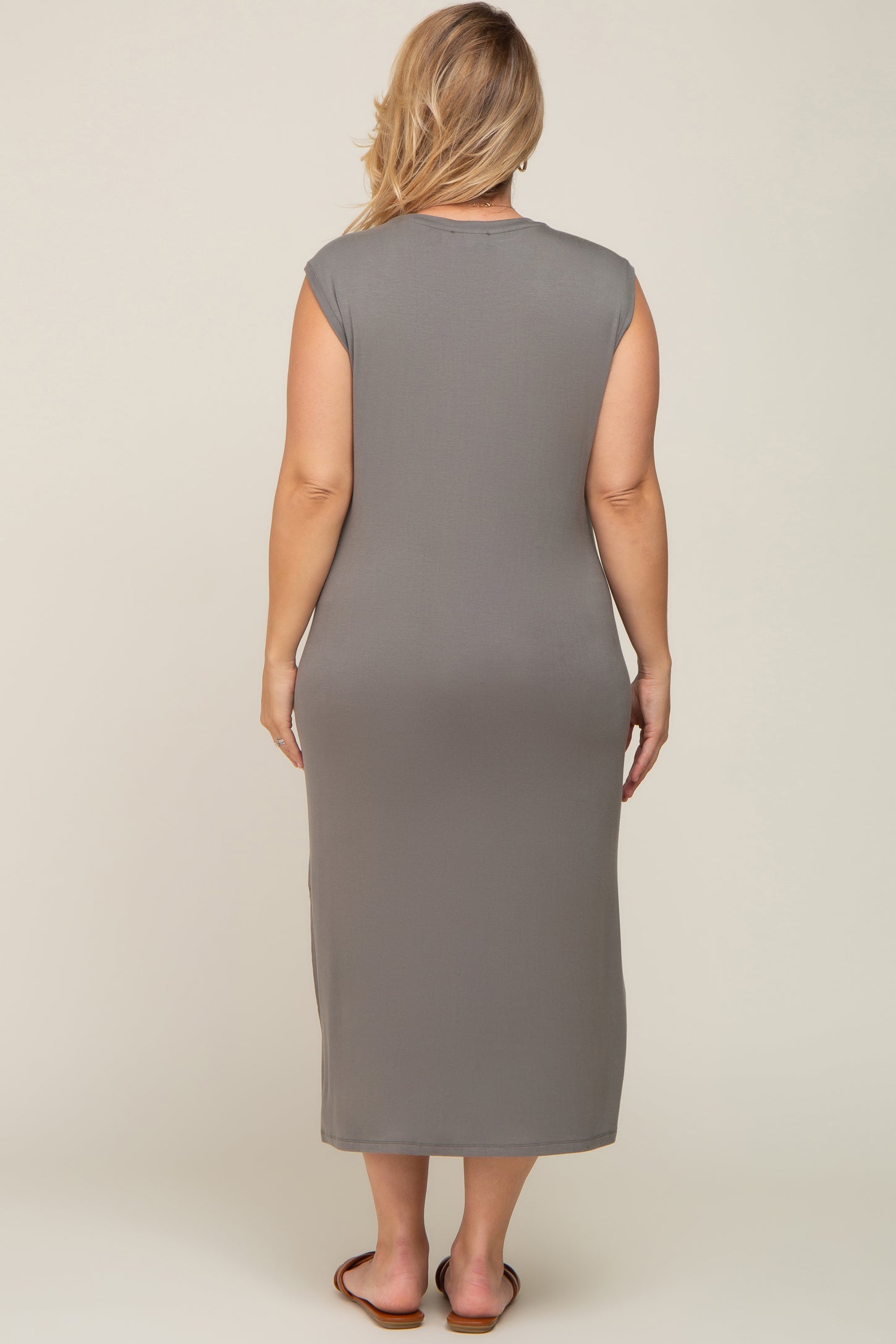 woman wearing a gray sleeveless maternity plus dress, showing the back view and a form-fitting silhouette