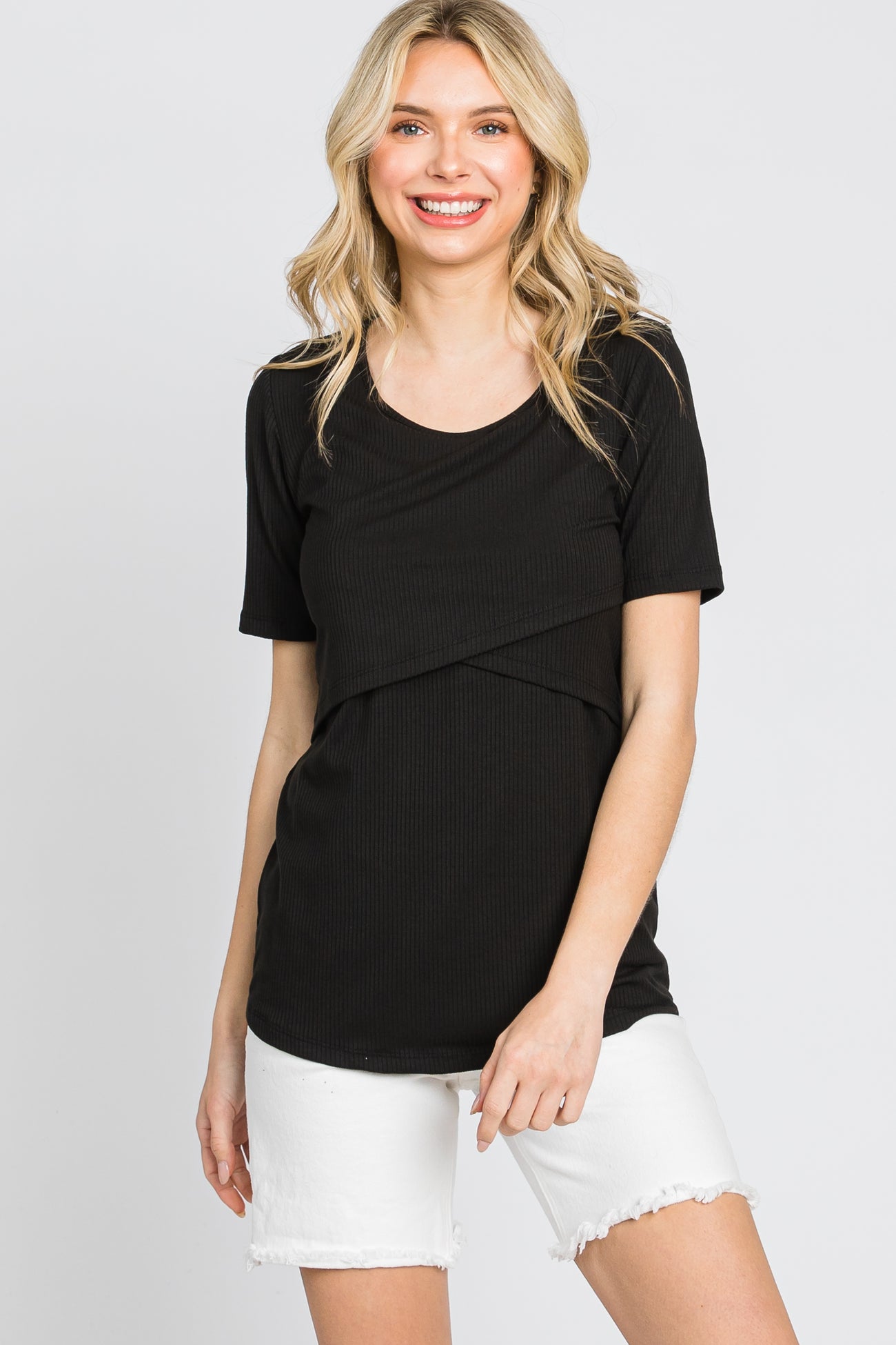woman wearing a black short sleeve top with a crossover front detail and white denim shorts