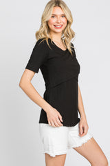 woman wearing a black short sleeve top with a layered design and paired with white distressed shorts
