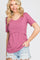 smiling woman wearing a mauve ribbed short sleeve top with crossover detail and distressed denim shorts