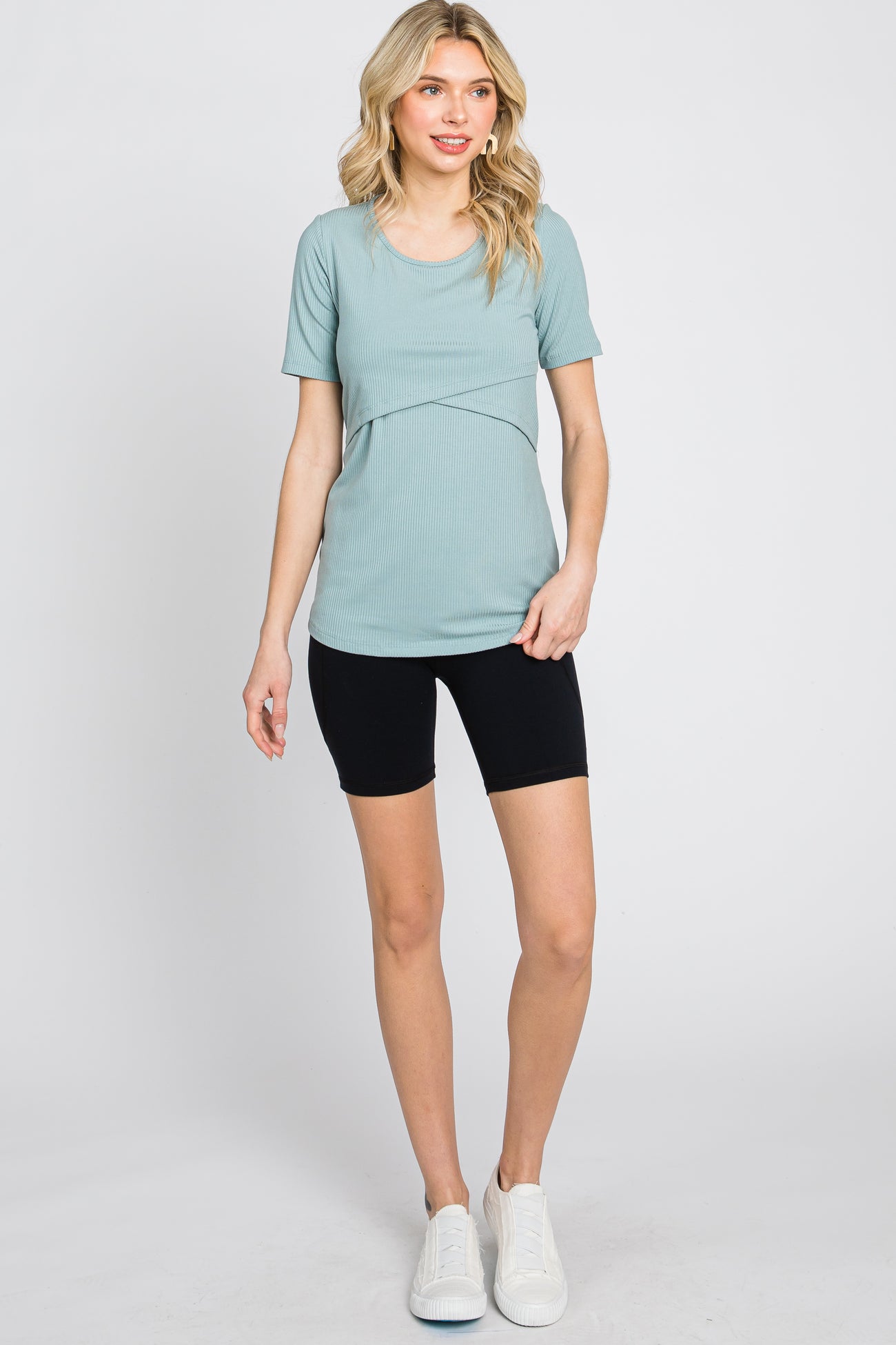 woman wearing a light teal short sleeve top with a twist detail and black bike shorts, standing with one hand on her hip
