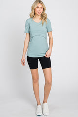 woman wearing a light teal short sleeve top with a twist detail and black bike shorts, standing with one hand on her hip