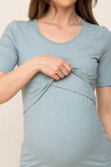 woman wearing a light blue short sleeve maternity top, pulling fabric to reveal a baby bump
