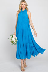 Woman in a sleeveless blue tiered maxi dress holding a bouquet of white roses against a white background