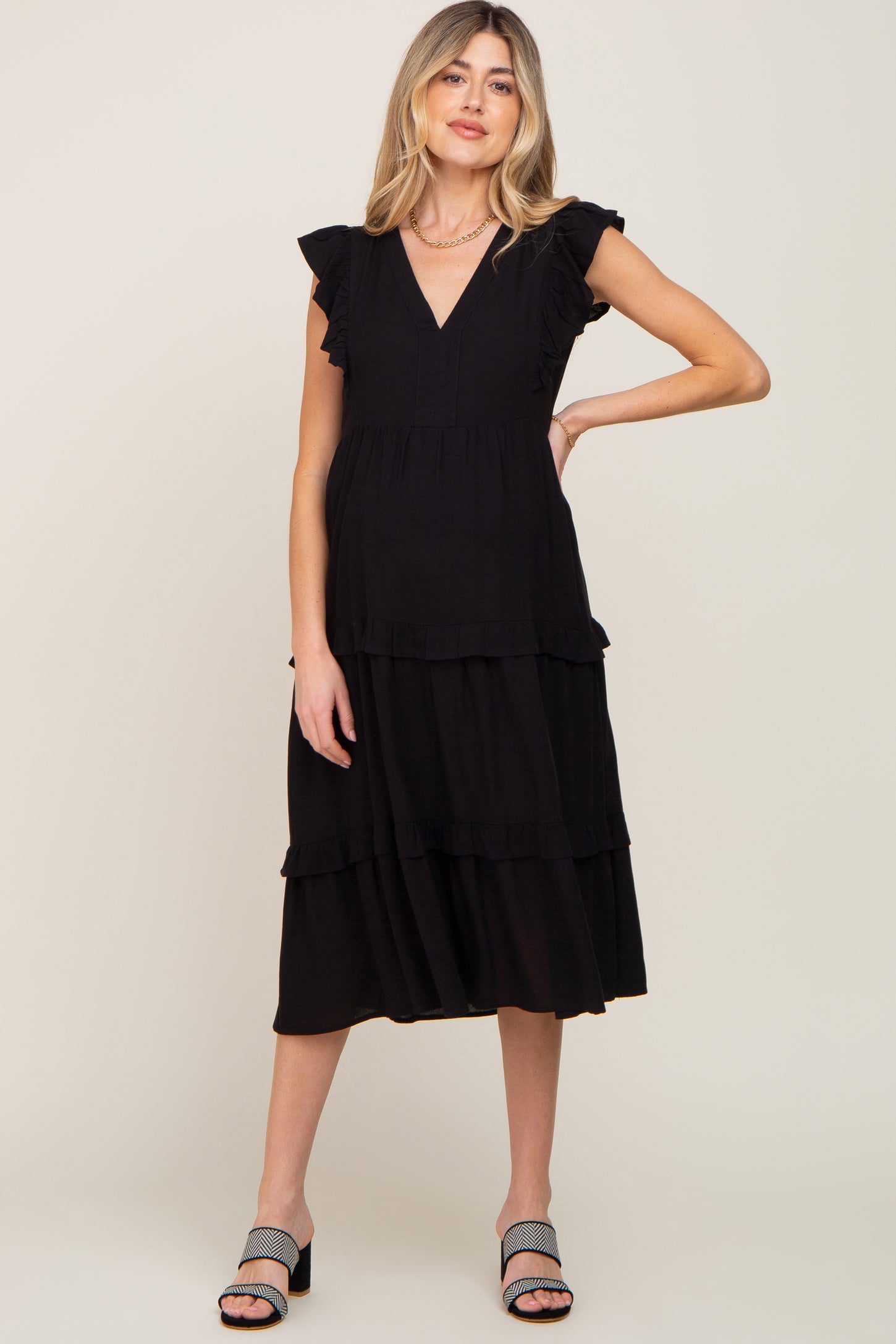 woman wearing a black tiered maternity midi dress with ruffle sleeves and a v-neckline