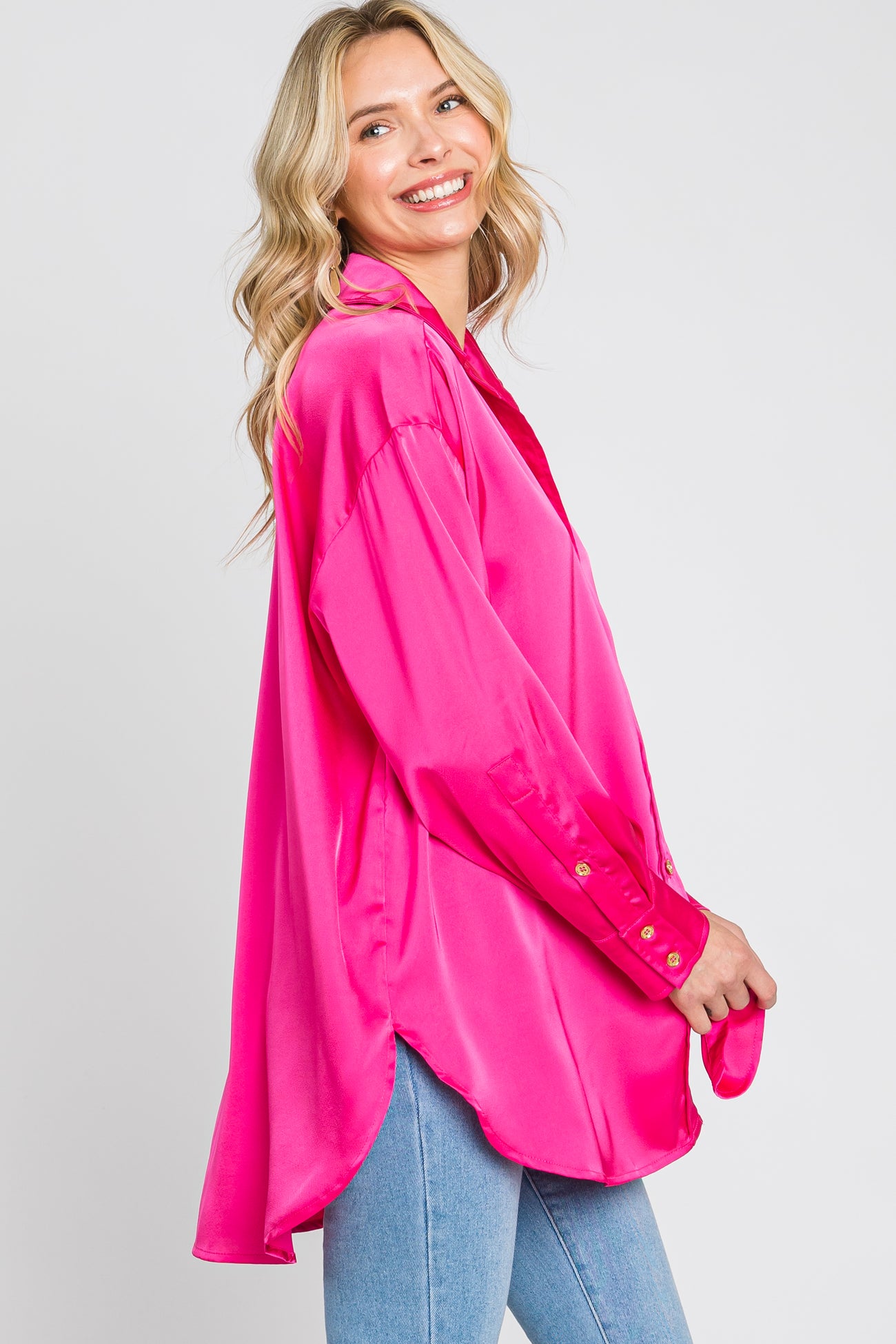 smiling woman wearing an oversized hot pink satin button-down shirt and blue jeans
