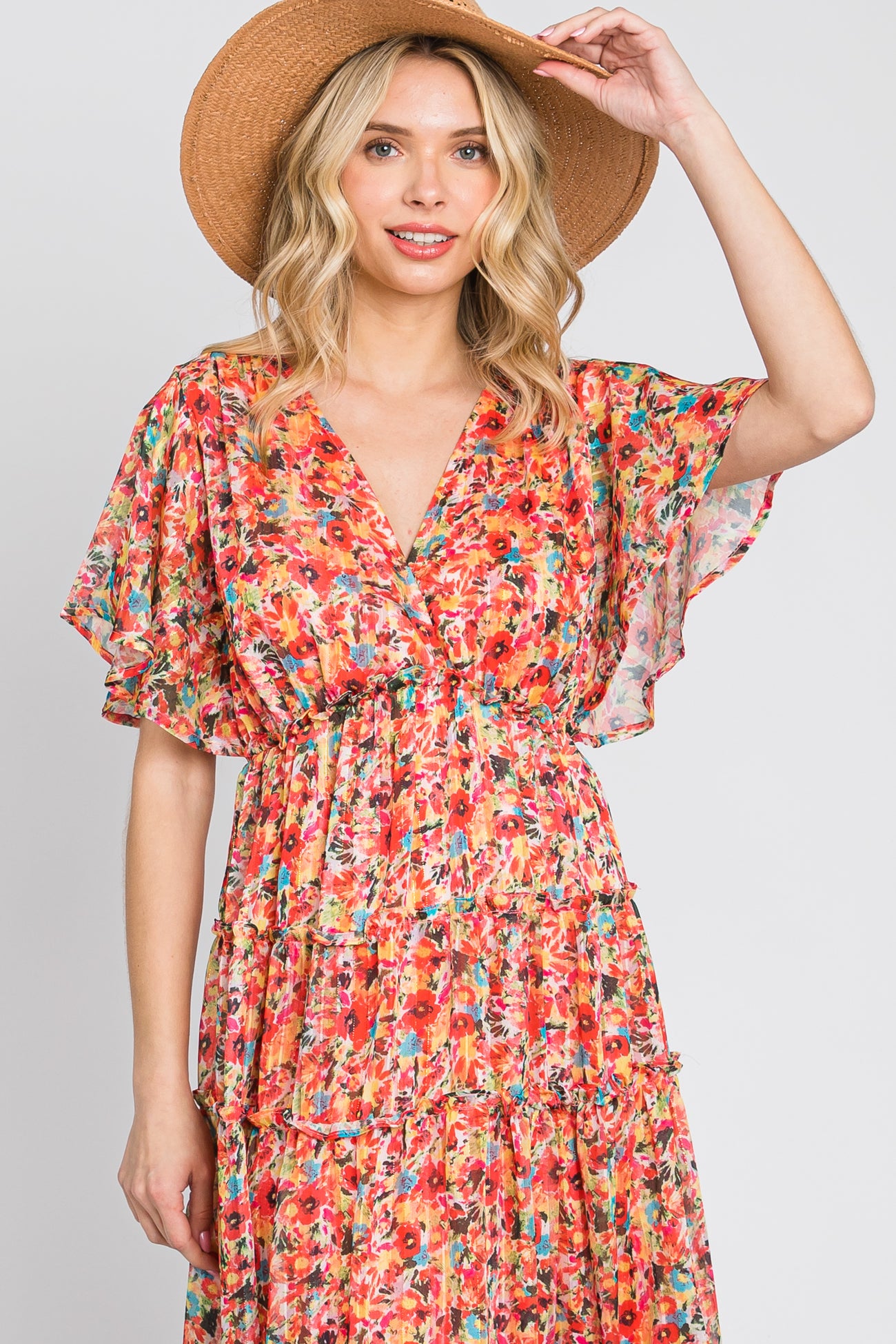 Woman wearing a colorful floral print v-neck dress and a tan straw sun hat against a white background