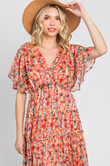 Woman wearing a colorful floral print v-neck dress and a tan straw sun hat against a white background