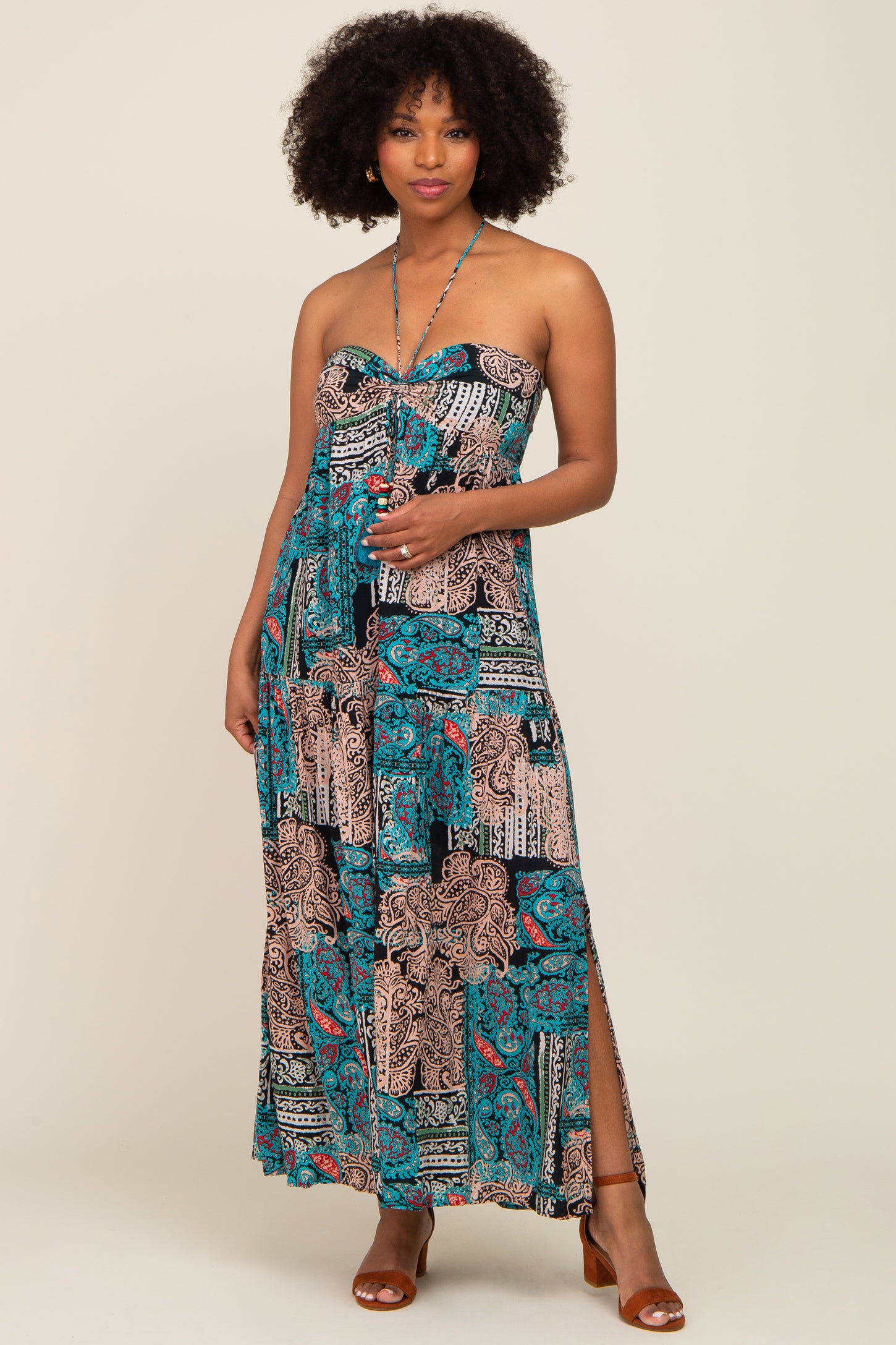 woman wearing a strapless maxi dress with a colorful paisley print and side slits, standing with one hand on her hip