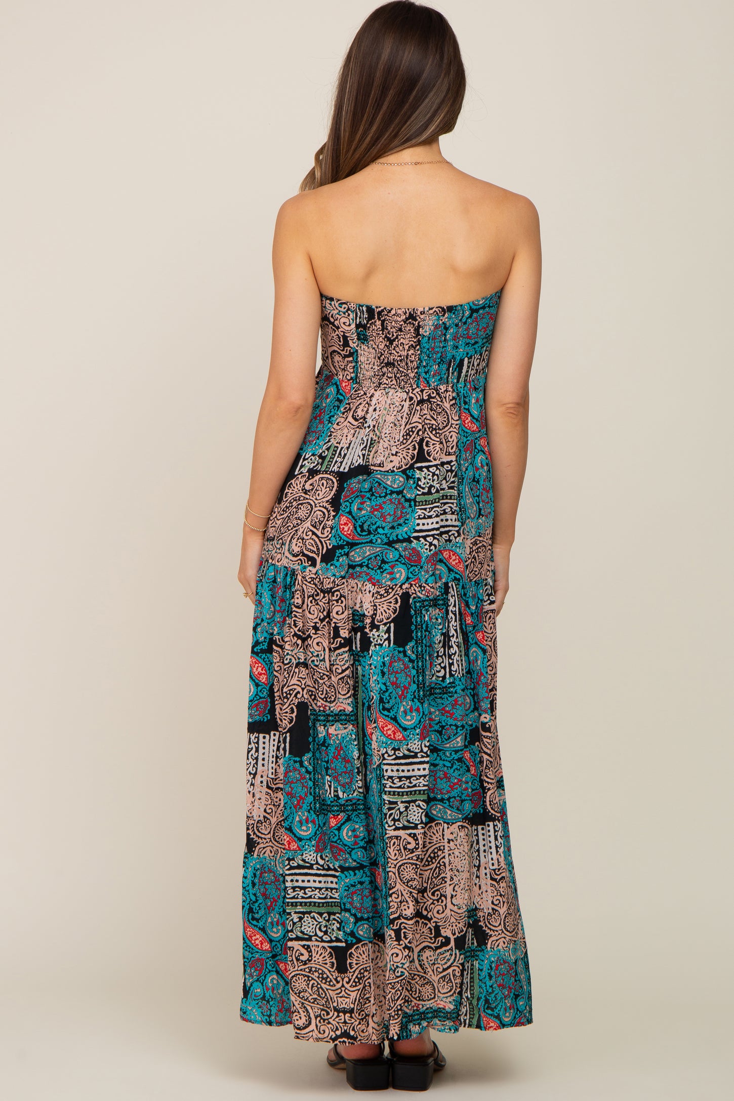 woman wearing a multi-colored strapless maternity maxi dress with a flowy skirt from the back