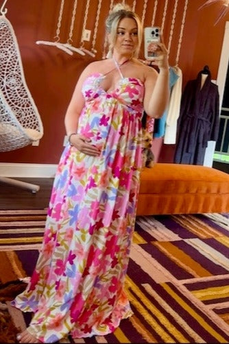pregnant woman in pink floral maxi dress taking a mirror selfie in a boutique