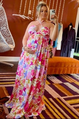 pregnant woman in pink floral maxi dress taking a mirror selfie in a boutique
