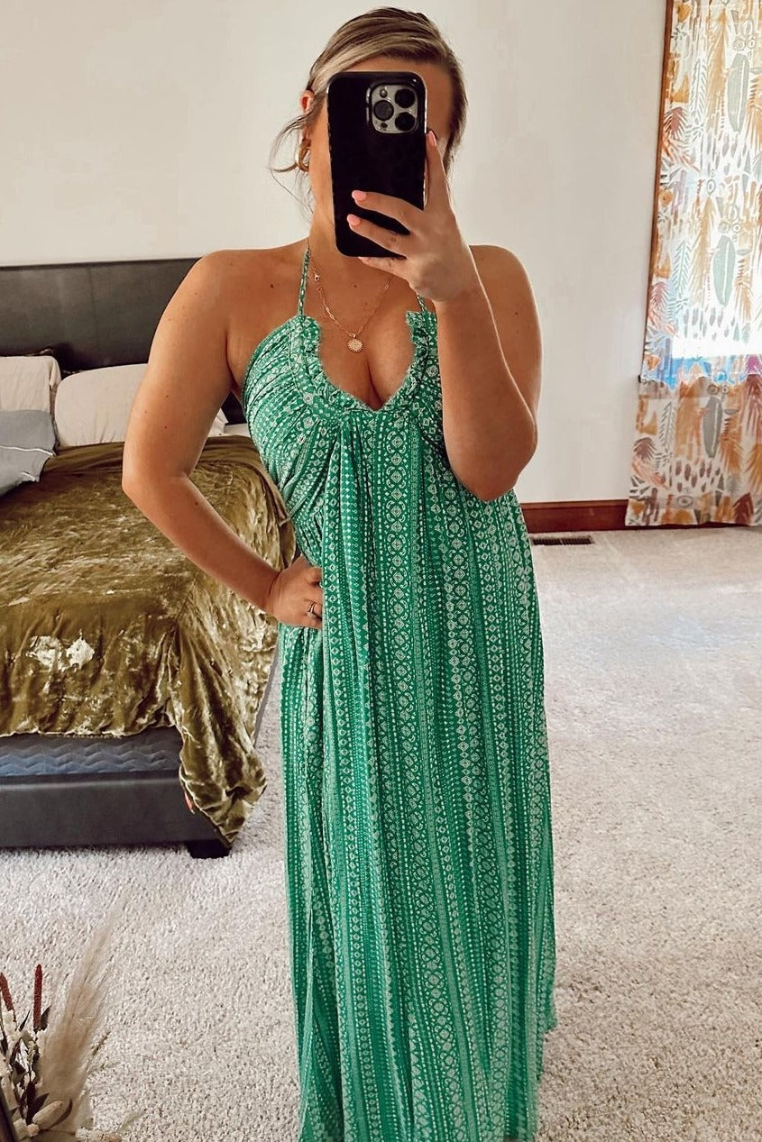 Woman taking mirror selfie wearing a green patterned halter neck maxi dress in a bedroom